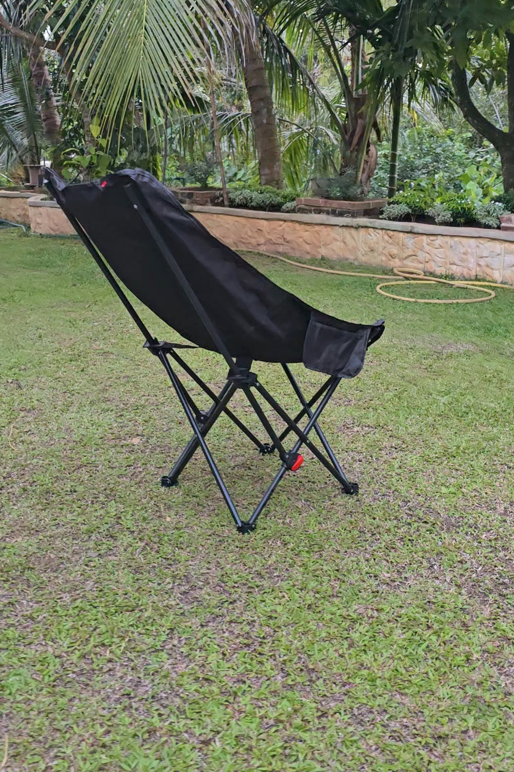 The black folding chair standing alone on a lawn beneath palms.