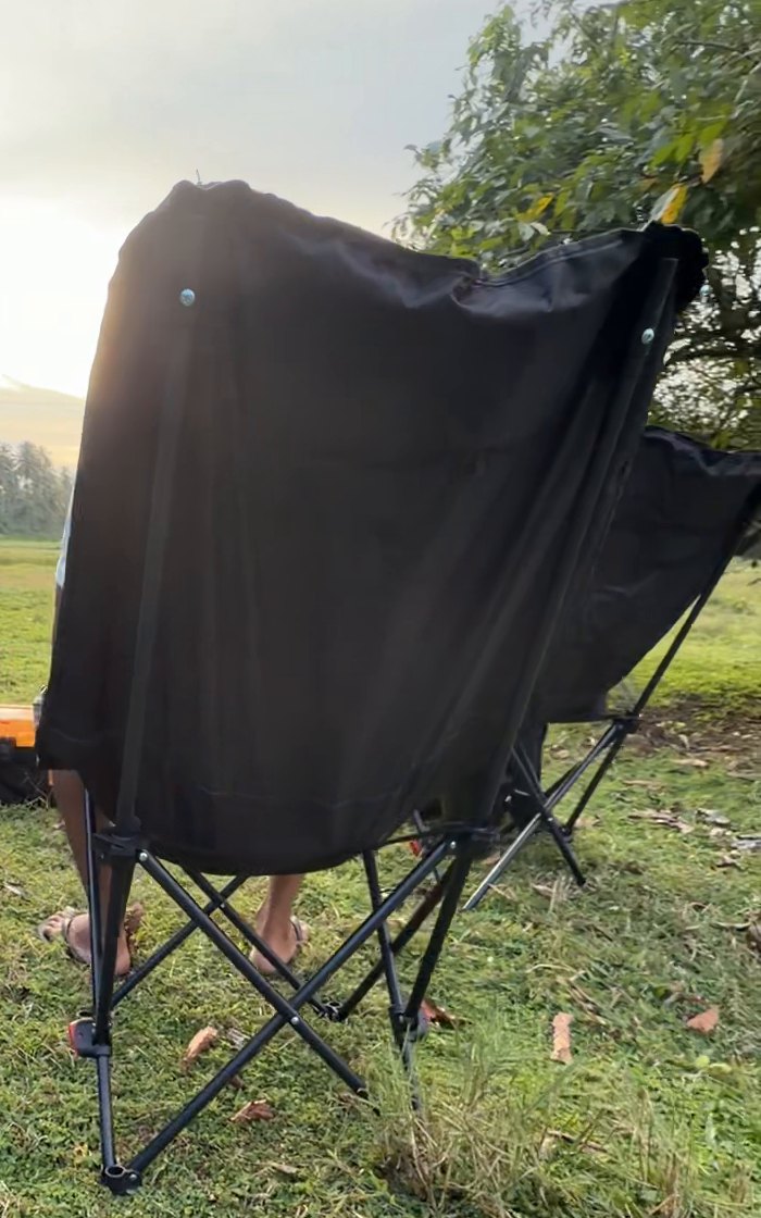 Black folding chairs seen from behind, facing an open field and trees in the evening light.