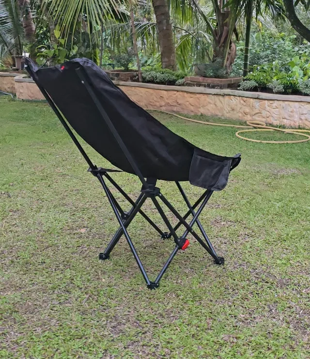 Side view of the open black folding chair on grass, showing its backrest and crossing frame.
